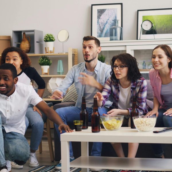Groupe d'amis regardant un match à la télévision dans un salon lumineux - convivialité streaming