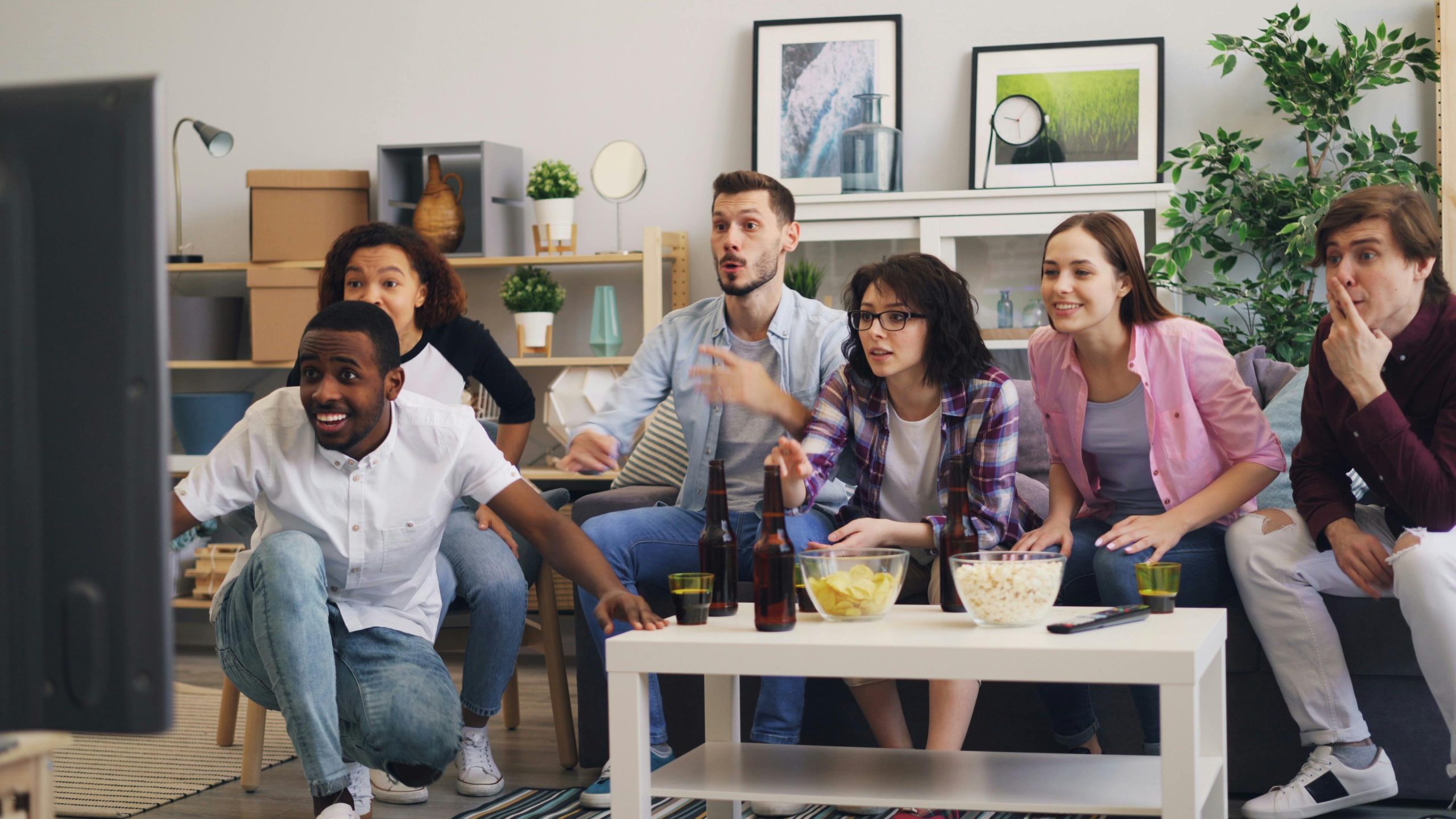 Group of friends watching a match on television in a bright living room - streaming conviviality