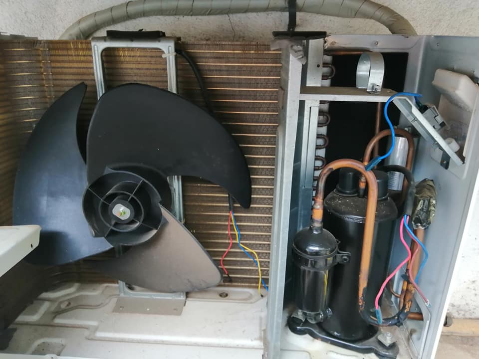Intérieur d’une unité extérieure de PAC air-air montrant compresseur, ventilateur et tubes cuivre