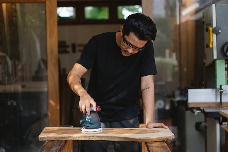 Professional woodworker using sander in indoor workshop, wearing protective goggles.